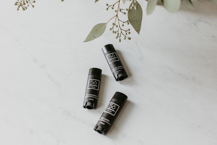 three of the same skincare products lying on a marble surface with some flowers