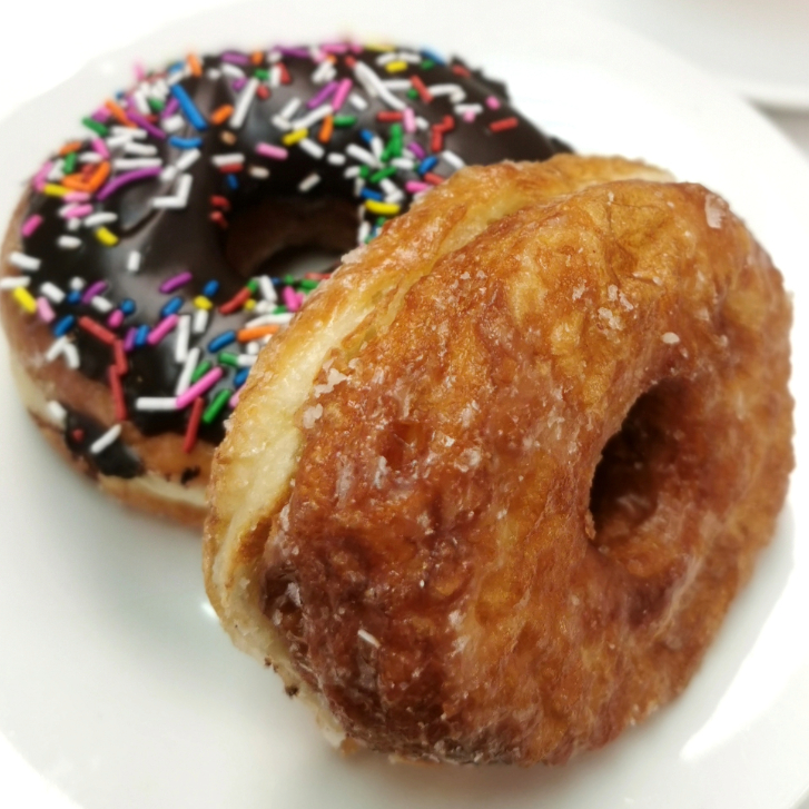 a chocolate-glazed donut with sprinkles and another donut leaning against one another
