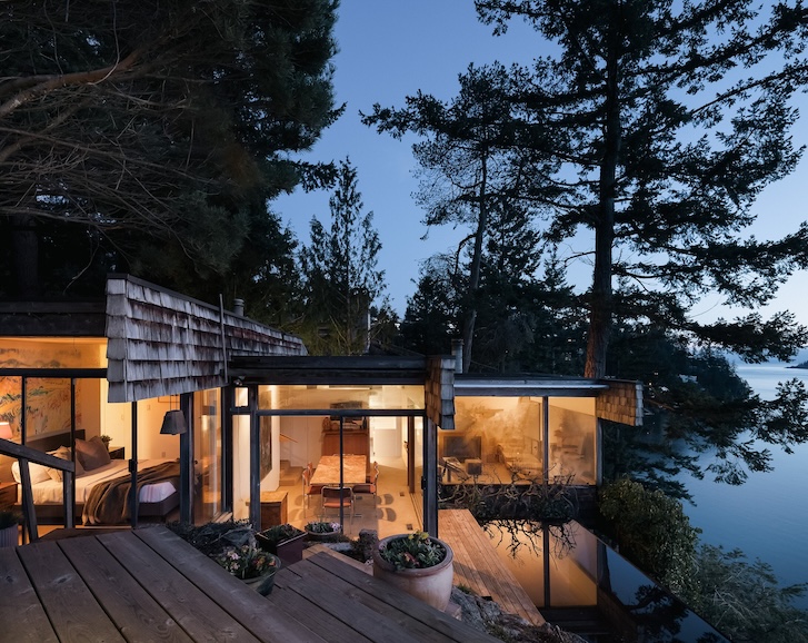 lit west coast house with pond connected to the deck, offering up beautiful contrasting textures with the orange skies and surrounding greenery.