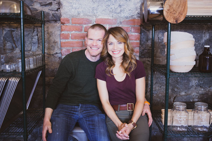 smiling man sitting closely to a smiling woman with his left hand around her waist