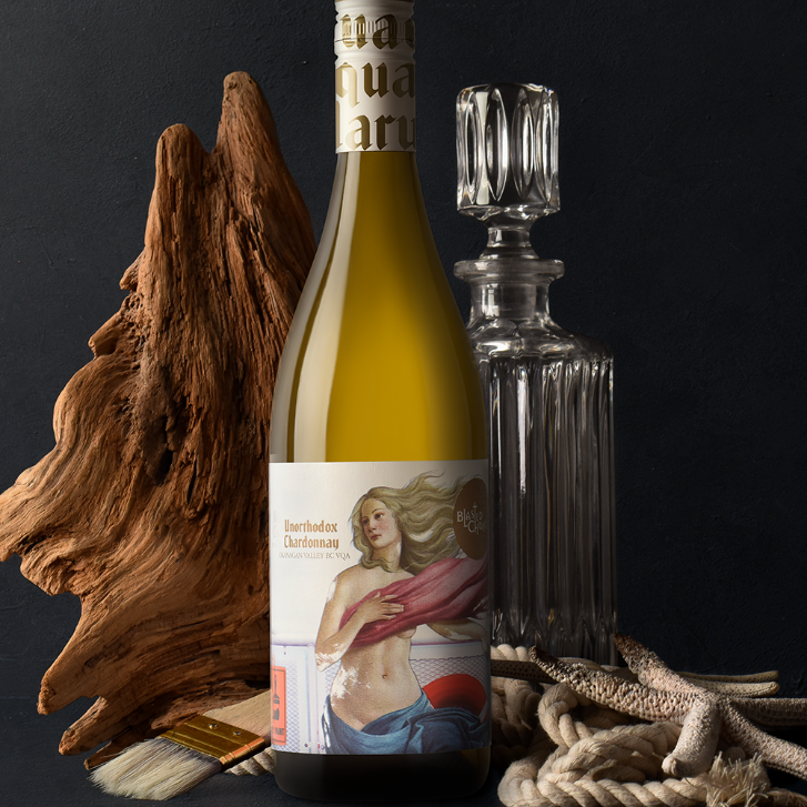 bottle of Unorthodox Chardonnay on a display with a piece of wood, decanter, and rope