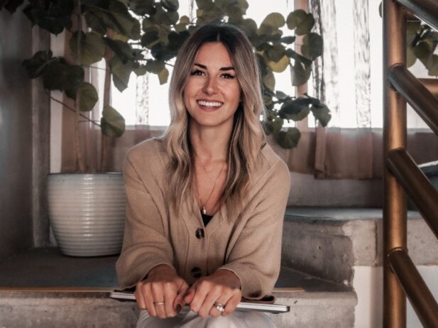 a smiling startups woman seated on steps holding a laptop on her knee with both hands