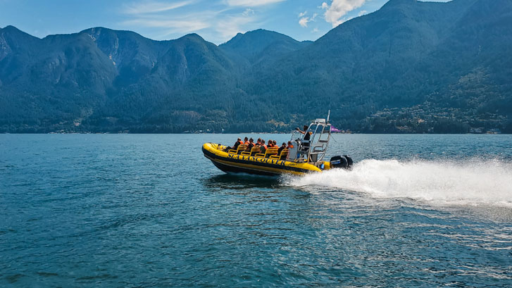 a boat riding on the sea with a group of people in life jackets on it and the high mountains in view