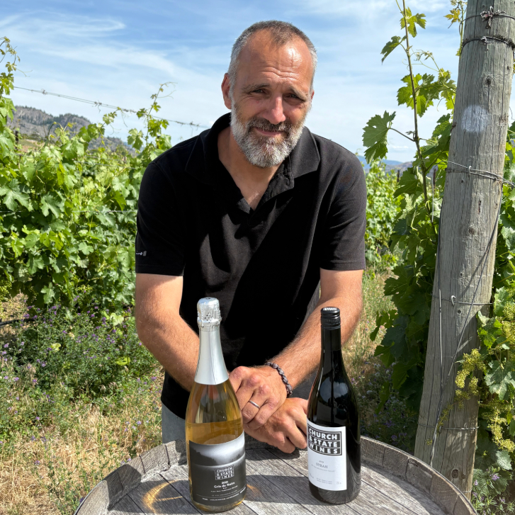 Church & State winemaker Arnaud Thierry posing in the vineyards with two bottles on a barrel
