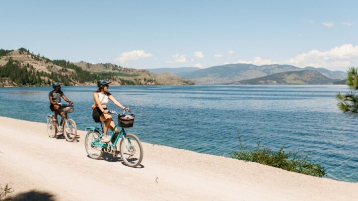 white girl and black guy riding bicycles by the beach of a huge river near