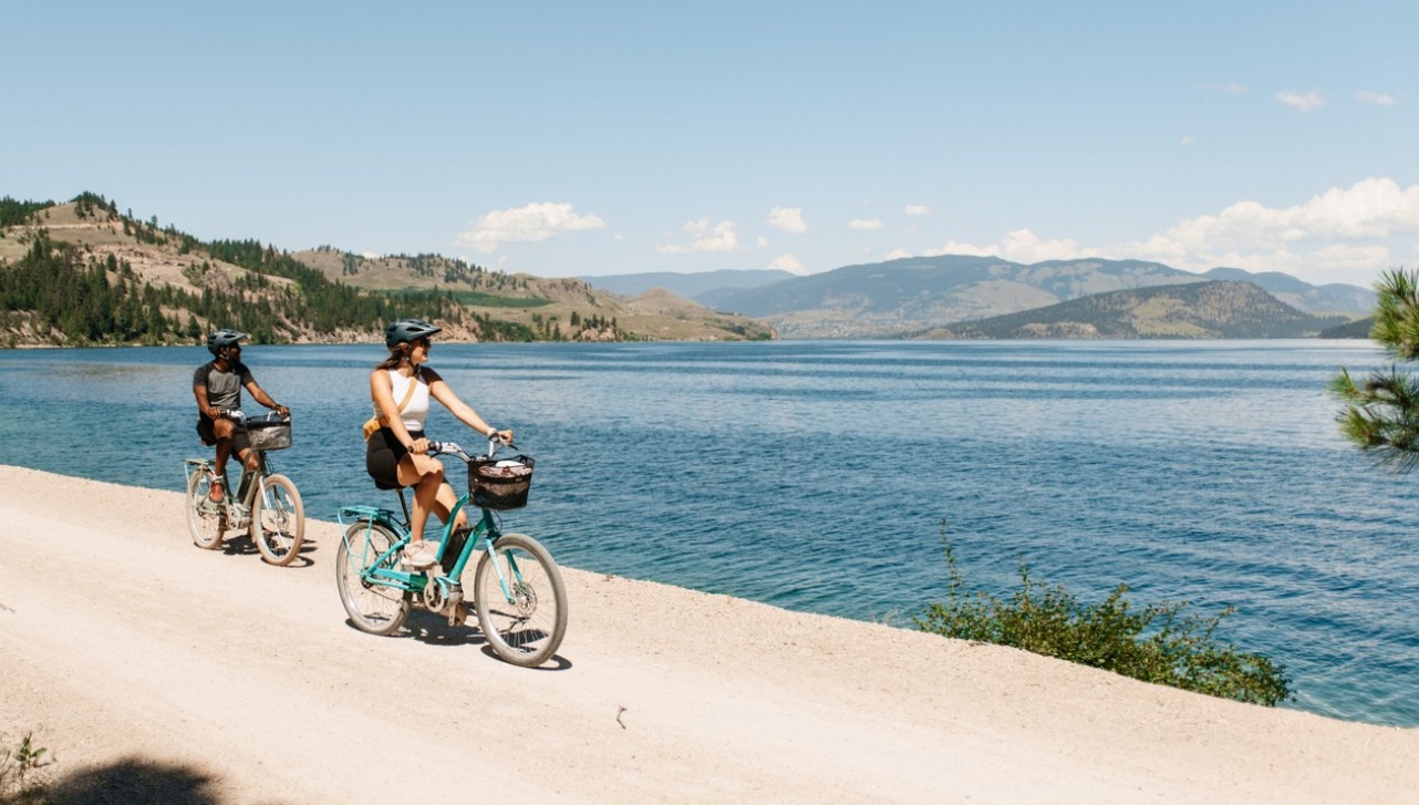 white girl and black guy riding bicycles by the beach of a huge river near