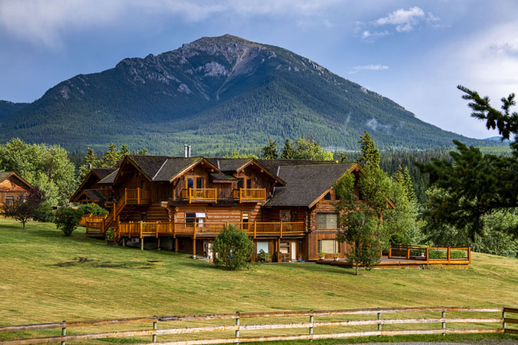 big wooden retreat lodge building with sparse green trees around and a huge mountain far behind