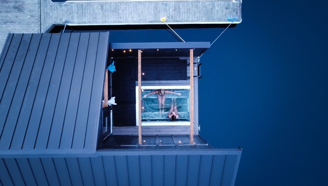 two ladies sitting inside a floating spa cryotherapy water tub within a small open roof housing on a lake