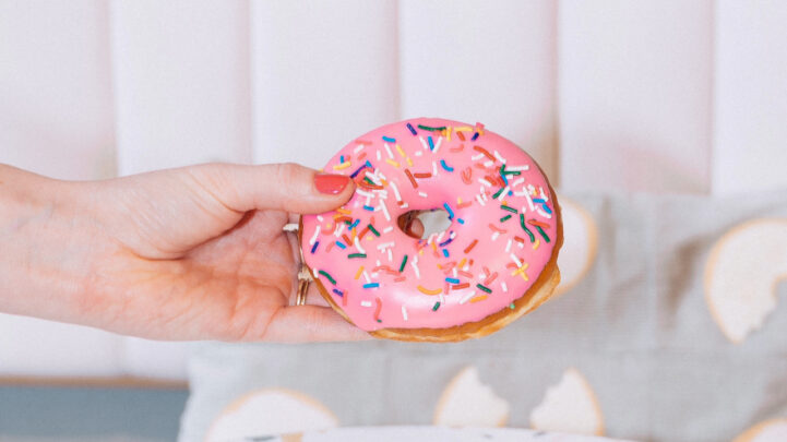 hand holding up a doughnut with pink icing and rainbow sprinkles