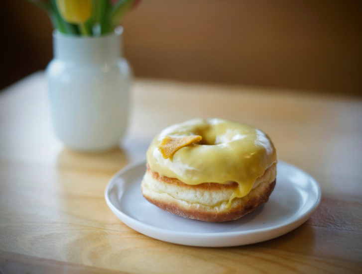 yellow glazed donut on a plate with a white vase in the background