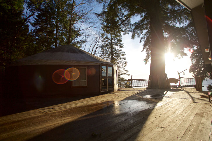 a building with a large wooden deck overlooking sunset and ocean and tall large trees above the building