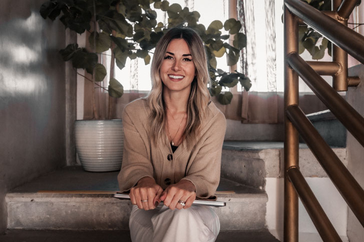 a smiling startups woman seated on steps holding a laptop on her knee with both hands