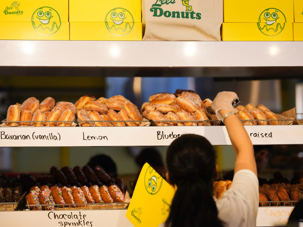 worker at Lee's Donuts grabbing a donut from the rack and holding a yellow box