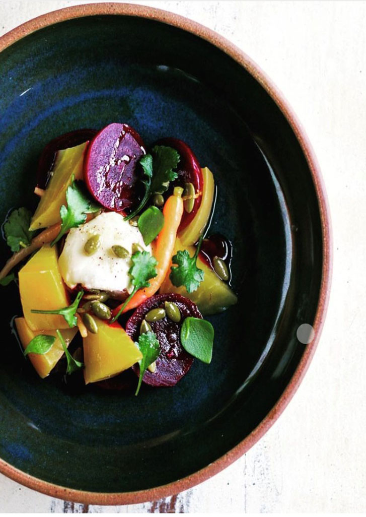 a plate of food containing cooked beets, small green leaves, and a yellow lump-like vegetable