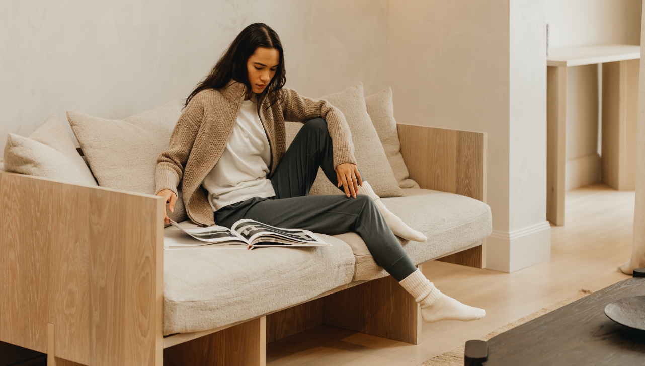 lady in a clothing brand sweaters and sweat pants while seated on a couch looking through a magazine