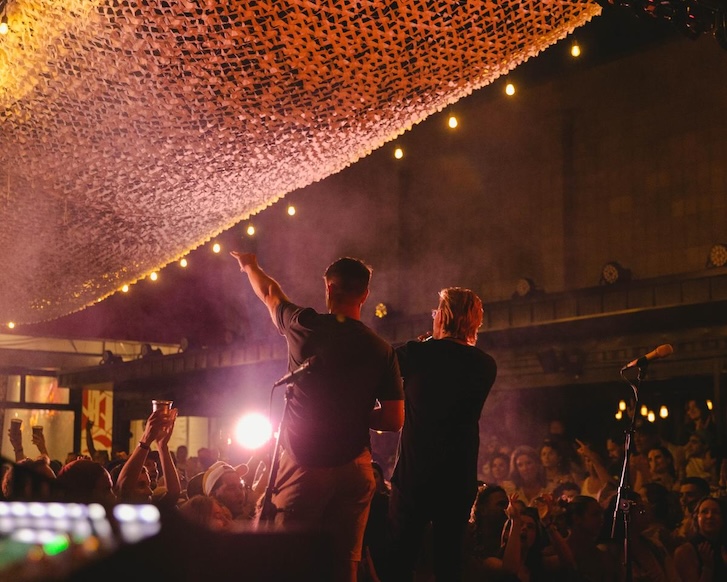 two men on a stage facing a huge crowd and one holding a mic