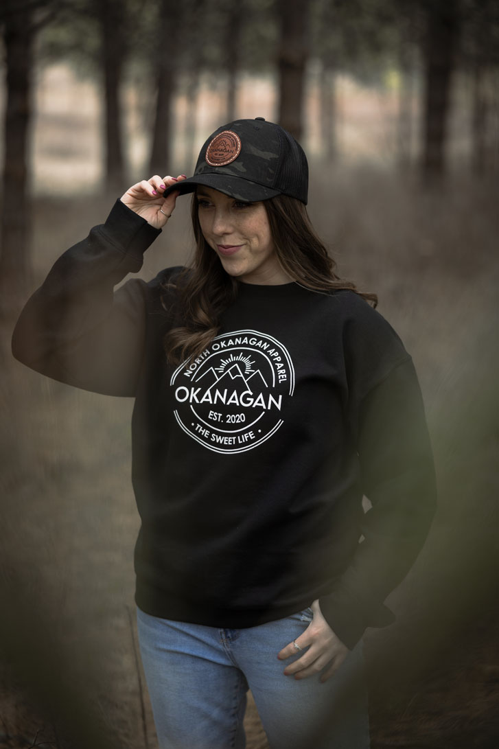 woman wearing a black facecap and a black crewneck sweatshirt with the words "Okanagan" on it