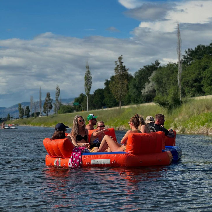 a group of friends seated on a round comfortable red pool floater on a lake