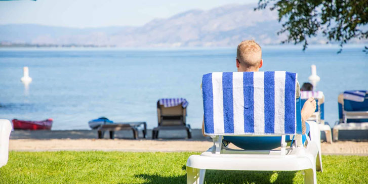 man lying on a beach chair with his towel hanging behind him on the head of the chair and the chair facing the huge beach waters