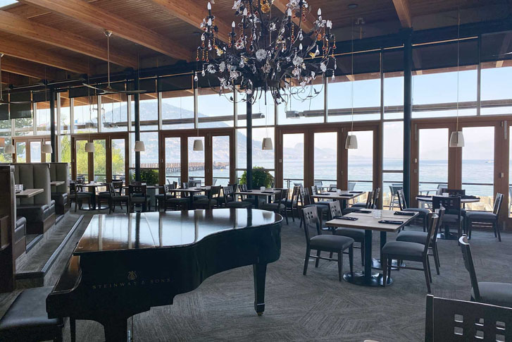 a big piano in a restaurant filled with groups of chairs and tables and transparent glass windows