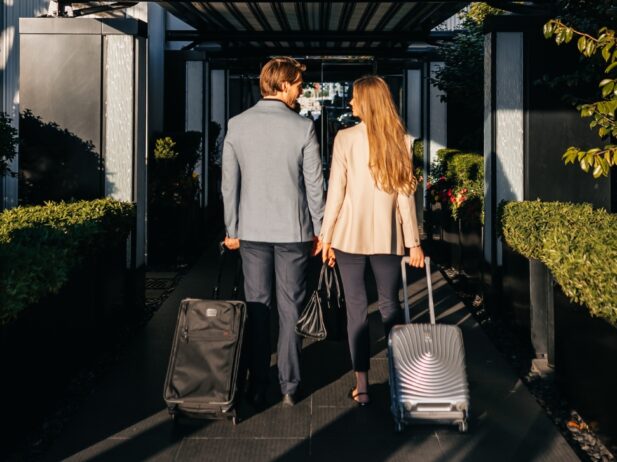 couple dressed corporate looking at each other while walking into a hotel resort and dragging their luggages behind them