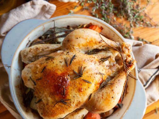 roasted whole chicken in a bowl with carrots and sprinkles of thyme over it