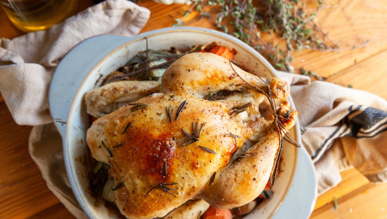 roasted whole chicken in a bowl with carrots and sprinkles of thyme over it