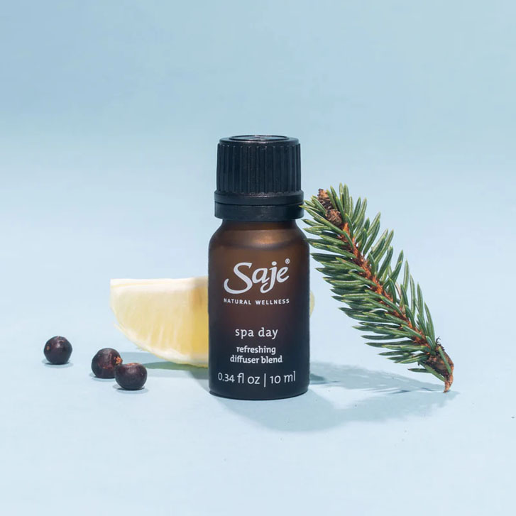 brown product bottle thats reads "Saje, spa day refreshing diffuser blend" with a leave and cut orange slice leaning beside it