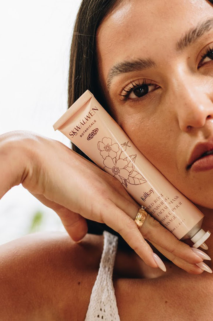 lady holds a Replenishing Facial Mask skin product close to her right cheek with the back of her right hand