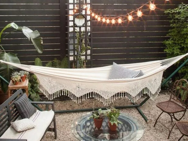 a hammock outside a yard with plants around, pot plants on a table and mini couches