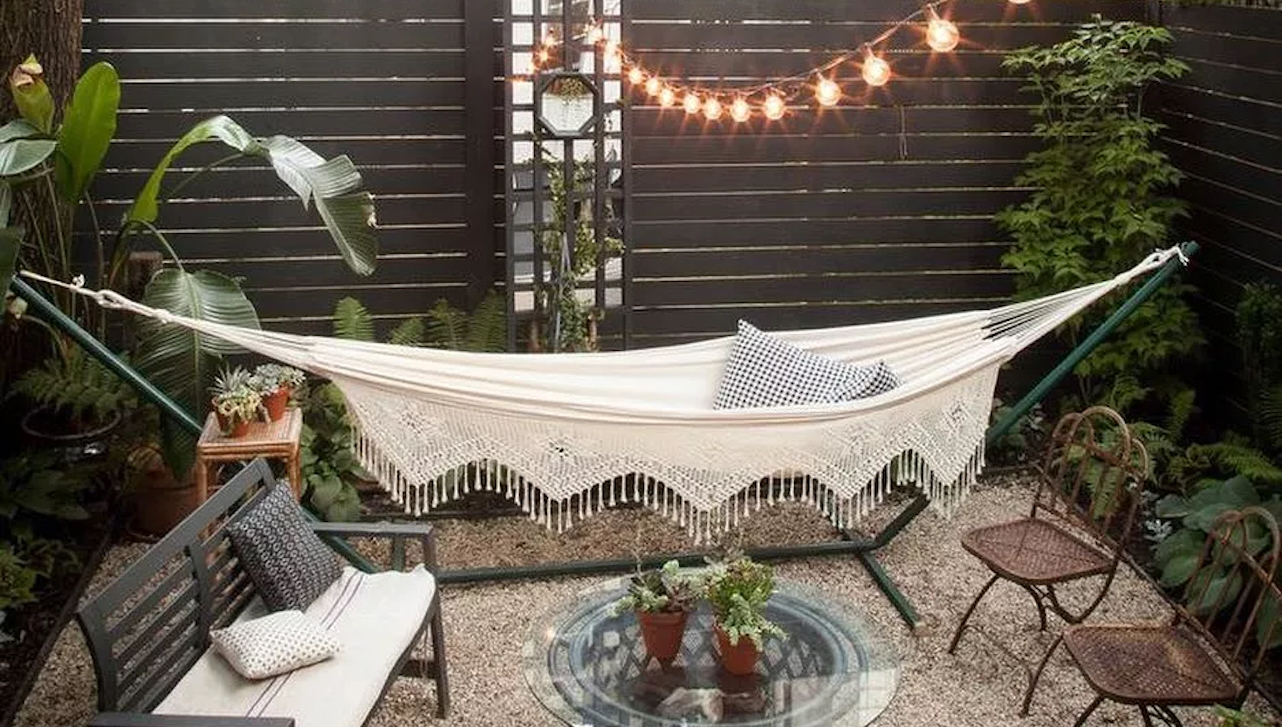 a hammock outside a yard with plants around, pot plants on a table and mini couches