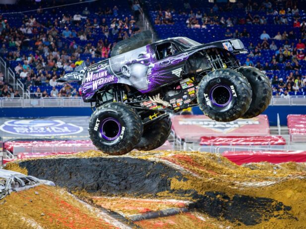 a truck ride car making a leap over sand on a monster jam ride stadium