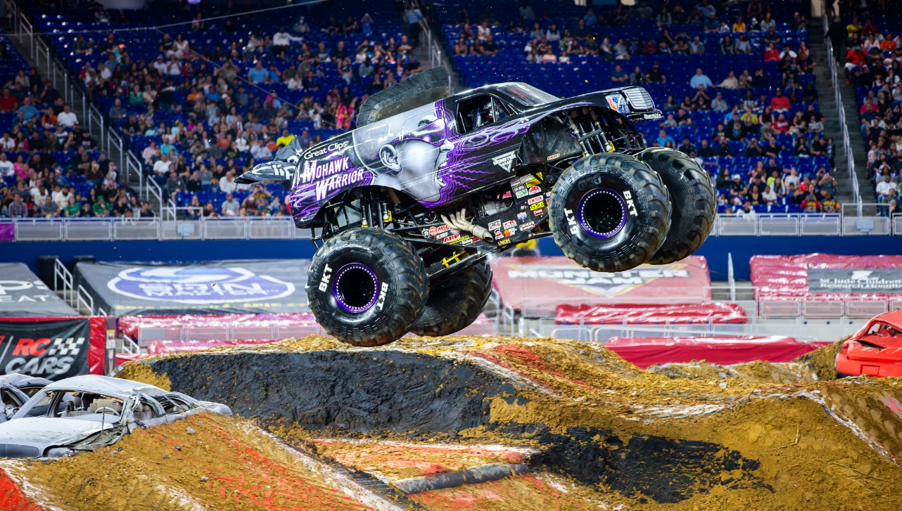 a truck ride car making a leap over sand on a monster jam ride stadium