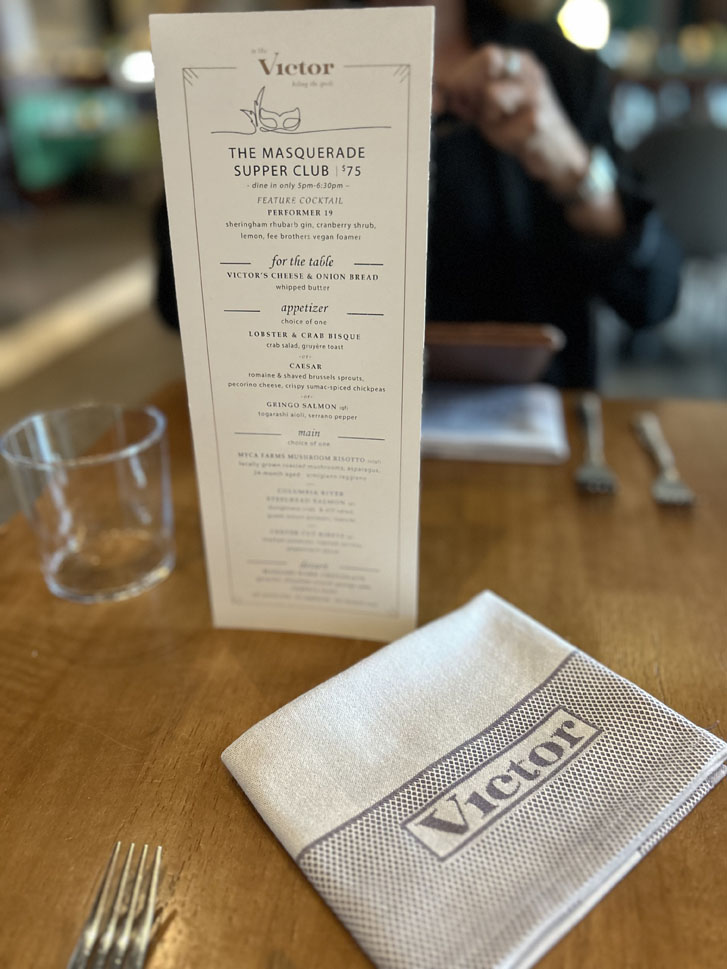 person in black seated at a restaurant table with a dinner menu and food cloth on the table