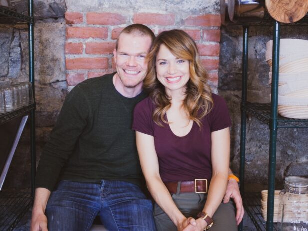 smiling man sitting closely to a smiling woman with his left hand around her waist