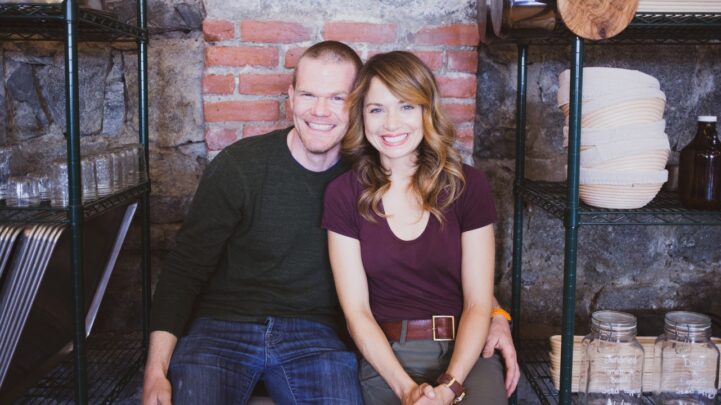 smiling man sitting closely to a smiling woman with his left hand around her waist