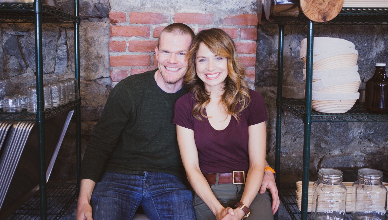 smiling man sitting closely to a smiling woman with his left hand around her waist