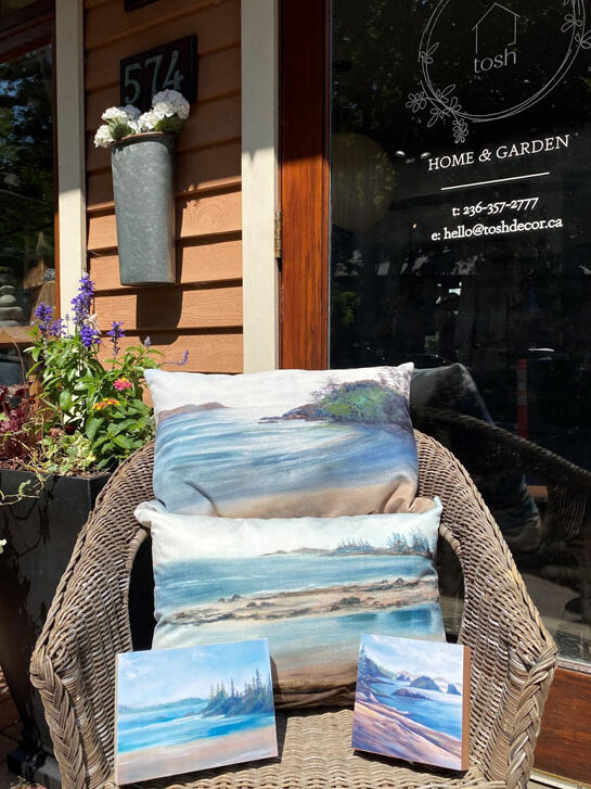 two handmade throw pillows and two ocean art canvases on a woven chair