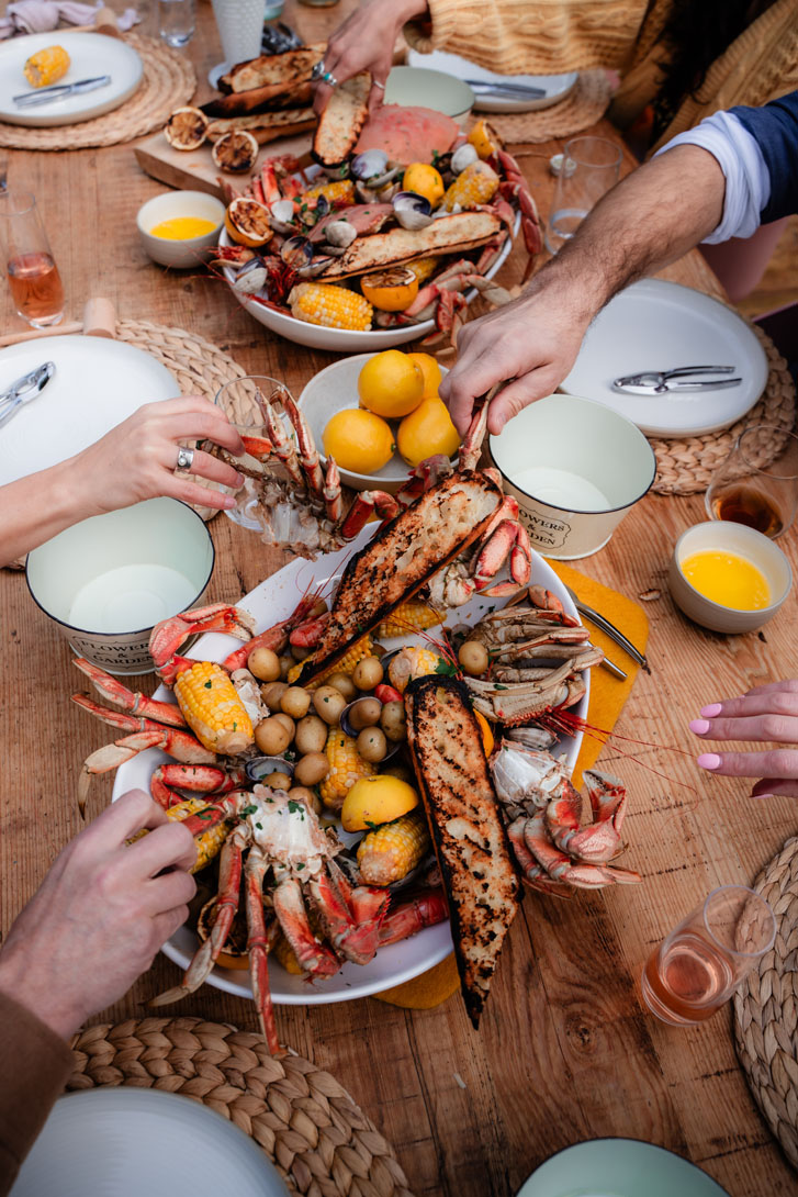 hands grabbing plates filled with crabs, corn, salmon fish, tiny potatoes and lemon slices