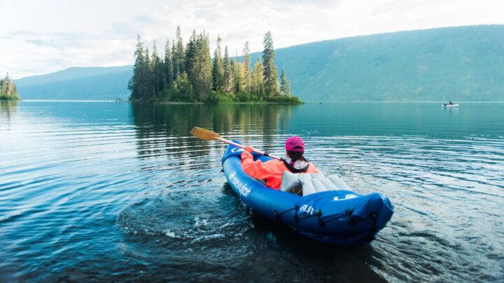 woman canoeing and kayaking with a paddle in her hand on a large lake with the hills around