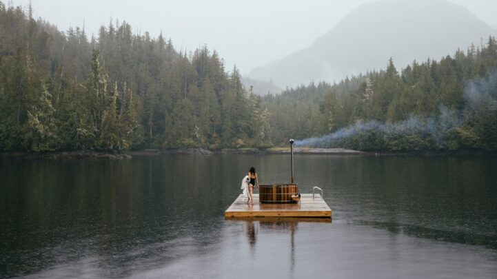 woman in a swimsuit holding a towel and walking around a wooden raft on a huge lake by the rainforest and hills