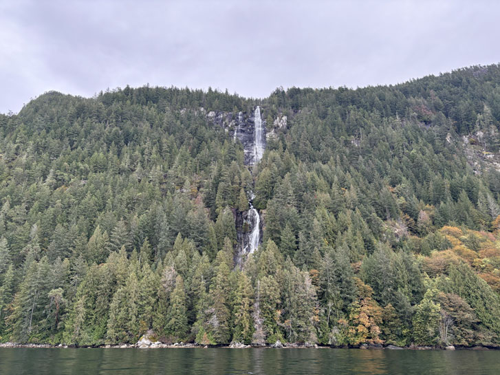 waterfall falling from between the green hills into the ocean