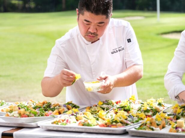 a chef in white placing vegetables on trays of food