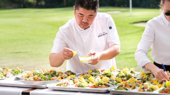 a chef in white placing vegetables on trays of food