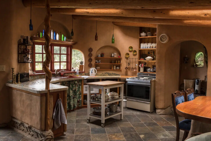 a kitchen featuring a beautiful stone countertop with mosaic details throughout and colourful glass bottles hanging from the ceiling above the counter, acting as lamp shades