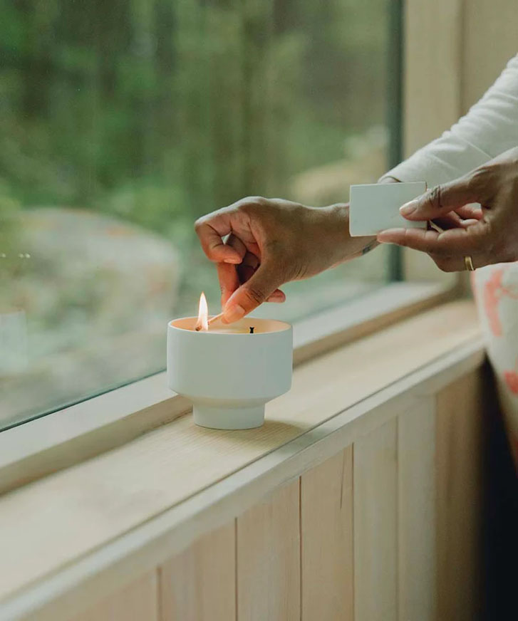 woman hand lighting a candle in an open cup-like glass at a transparent glass window