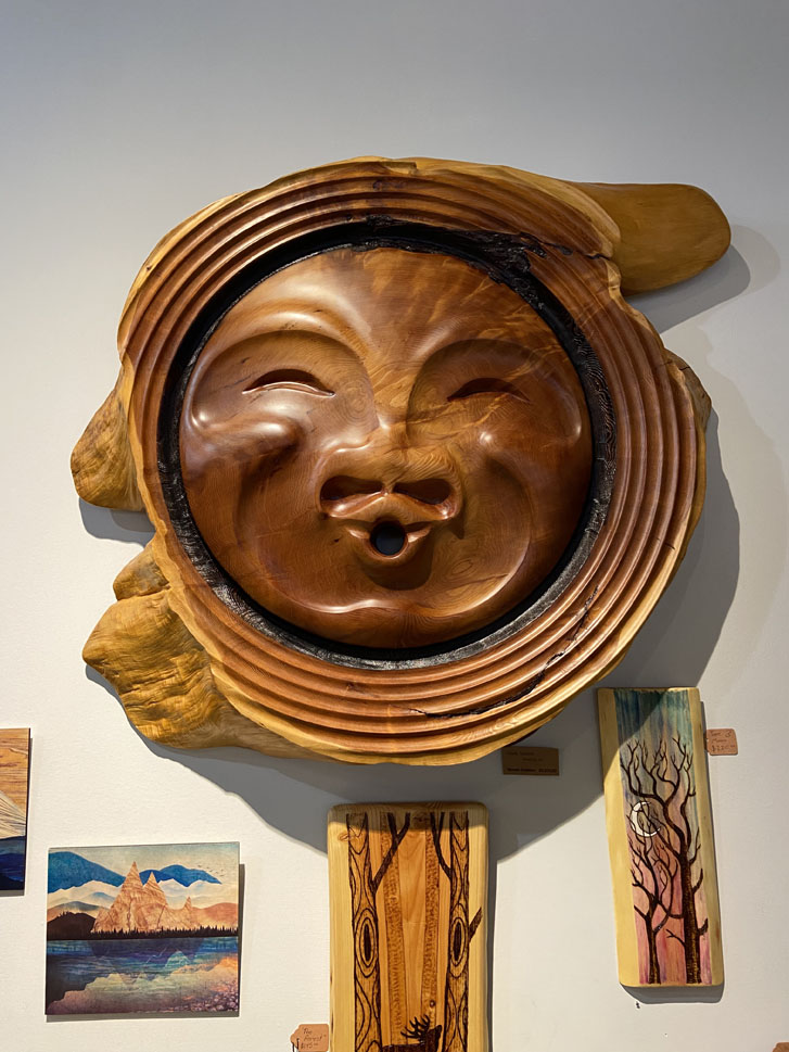 a whimsical face wooden carving hanging on the wall of a home decor shop