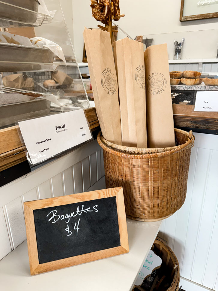 a basket of bagged Baguettes with the price beside it on a small black chalk board