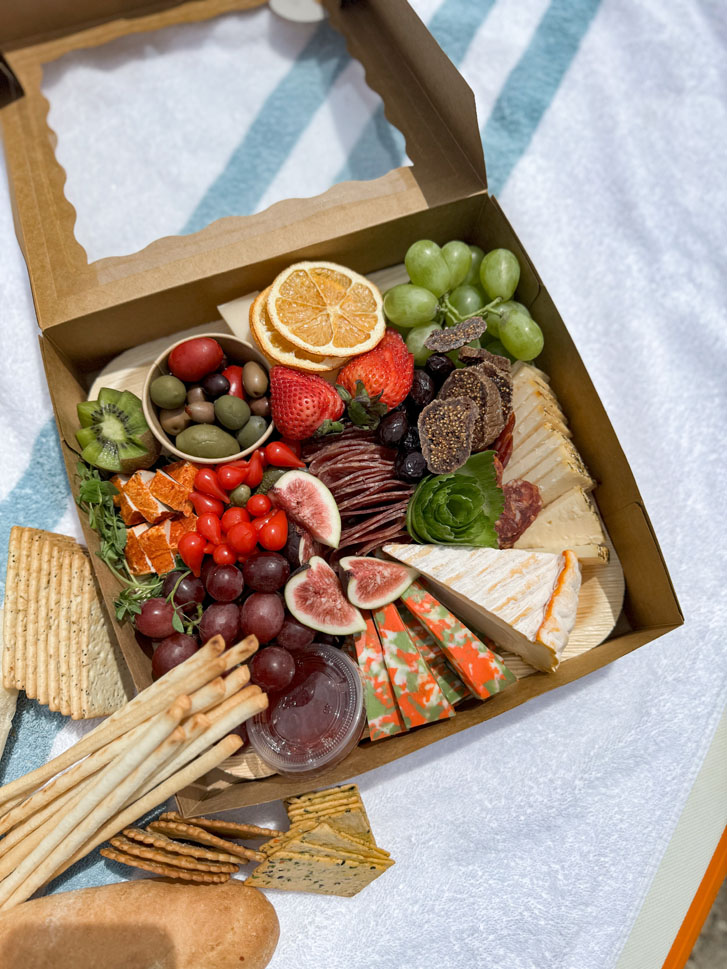 a super fresh charcuterie box with cheese, grapes, tomatoes, strawberries, ham and other veggies