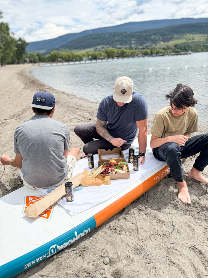 2 boys and a man sitting on a paddle board easting from a charcuterie board